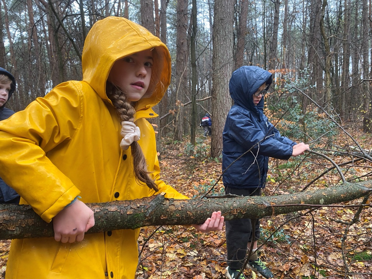 Twee kinderen in regenjassen tillen samen een tak op in het bos